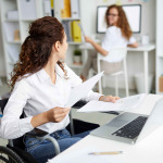 woman in wheelchair working with coworker in the office