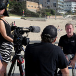 Two people operate a camera outdoor film shoot, actor in wheelchair