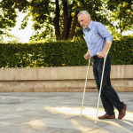 Man strolls in park with crutches, during a therapy