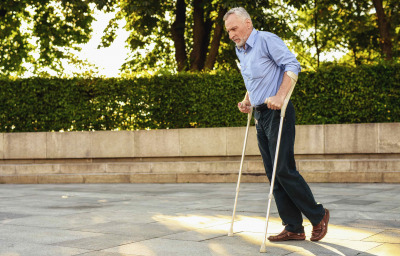 Man strolls in park with crutches, during a therapy