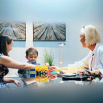 Pediatrician with mom and young boy with autism in medical clinic, playing with toys.