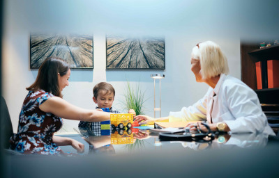 Pediatrician with mom and young boy with autism in medical clinic, playing with toys.