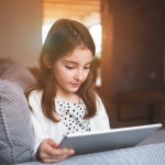 A happy small girl with tablet at home.