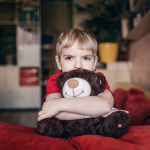Little boy hugging his teddy bear with sad feelings