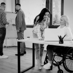 Side view of woman in wheelchair conversing with female coworker at the office