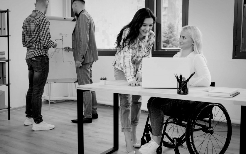 Side view of woman in wheelchair conversing with female coworker at the office