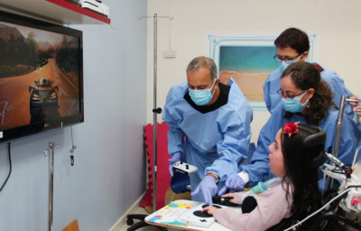 Microsoft's Yaron Galinsky with ALYN's Dr. Maurit Beeri and Arie Yekel-Melamed are seen helping a patient play 'Forza Horizon 4' on the Xbox One using an Xbox Adaptive Controller.