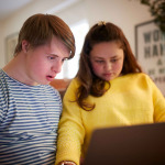 Young Downs Syndrome Couple Sitting On Sofa Using Laptop At Home