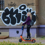 Young woman with headphones riding with electric scooter on pavement in the city.