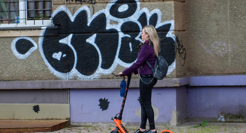 Young woman with headphones riding with electric scooter on pavement in the city.