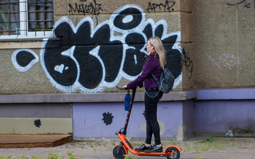 Young woman with headphones riding with electric scooter on pavement in the city.