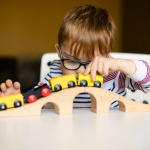 boy in the glasses with disability playing with wooden railways