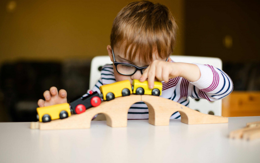 boy in the glasses with disability playing with wooden railways