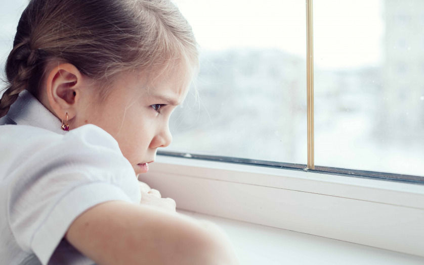 one sad little girl sitting near the window at the day time.