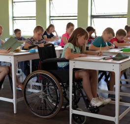 Side view of a diverse group of schoolchildren sitting at desks in classroom, with one schoolgirl sitting in a wheelchair