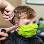 little boy getting hair cut at the barbershop wearing protective mask
