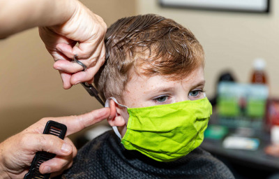 little boy getting hair cut at the barbershop wearing protective mask