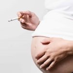 Anonymous pregnant woman with smoking cigarette in her hand other hand on the abdomen