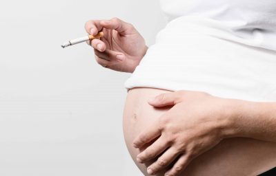 Anonymous pregnant woman with smoking cigarette in her hand other hand on the abdomen