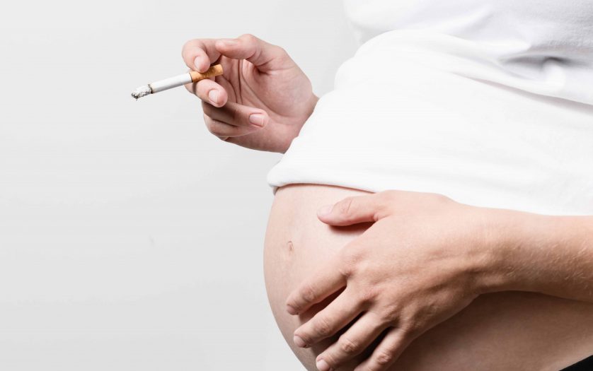 Anonymous pregnant woman with smoking cigarette in her hand other hand on the abdomen