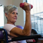Senior woman in wheelchair performing exercise with dumbbell
