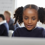 Young black schoolgirl using a laptop computer sitting at desk in a primary school classroom