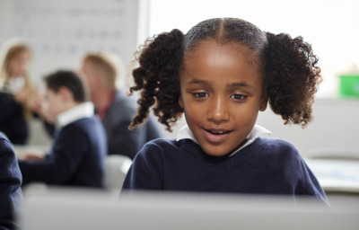 Young black schoolgirl using a laptop computer sitting at desk in a primary school classroom