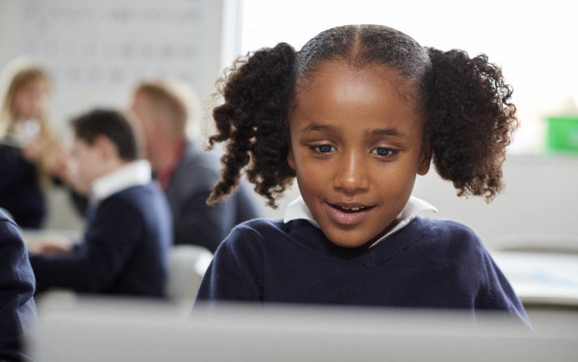 Young black schoolgirl using a laptop computer sitting at desk in a primary school classroom