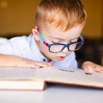 Boy with down syndrome with big glasses reading book