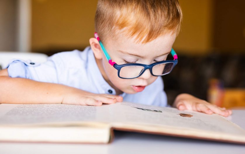 Boy with down syndrome with big glasses reading book