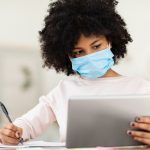 African American Kid In Face Mask Using Tablet Computer Learning Online Doing Homework At Home.