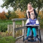 A disabled girl in a wheelchair relaxing outside together with a care assistant