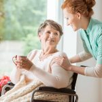 A professional caretaker in uniform helping a geriatric female patient on a wheelchair