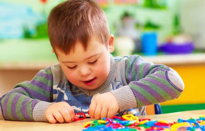 Cute kid boy with down`s syndrome playing in kindergarten