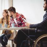 Coworker in wheelchair using digital tablet against photo editors in meeting room at creative office