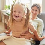 Portrait of cute girl with down syndrome laughing happily while playing with mother at home