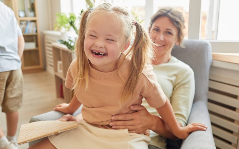 Portrait of cute girl with down syndrome laughing happily while playing with mother at home
