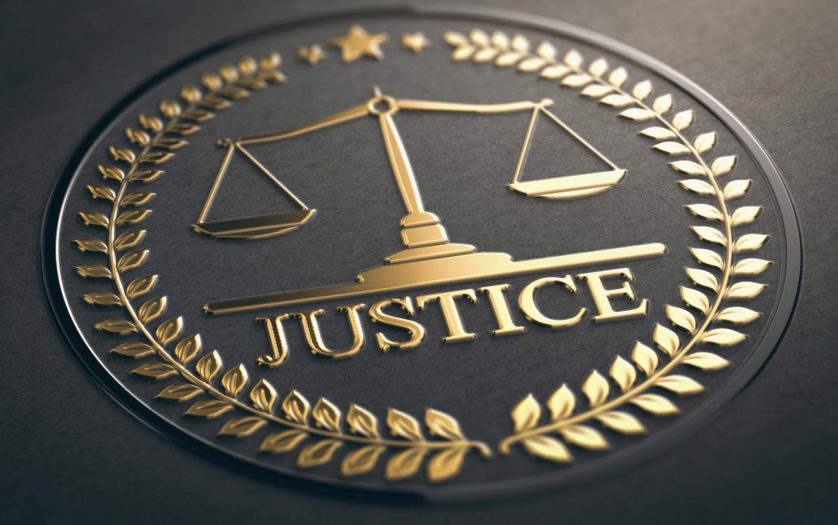 Scales of justice embossed symbol design with golden foil over black paper background.