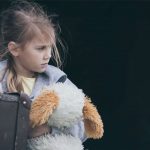 Portrait of young little girl sitting with suitcase outdoors at the day time