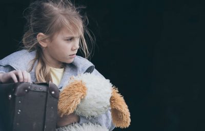 Portrait of young little girl sitting with suitcase outdoors at the day time