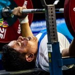 A male powerlifter competing being observed by a man in a chair