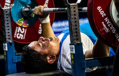 A male powerlifter competing being observed by a man in a chair