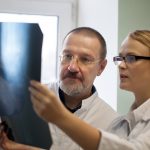 Young and experienced doctors looking at two x-ray images and trying to make a right diagnosis