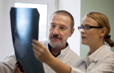 Young and experienced doctors looking at two x-ray images and trying to make a right diagnosis
