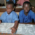 Schoolchildren writing with chalk on a slate
