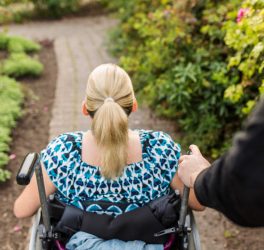 Disabled woman in wheelchair with assistant walking in garden