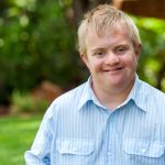 Portrait of handsome boy with Down syndrome in blue shirt outdoors.