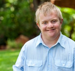 Portrait of handsome boy with Down syndrome in blue shirt outdoors.