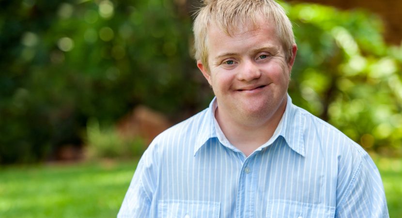 Portrait of handsome boy with Down syndrome in blue shirt outdoors.