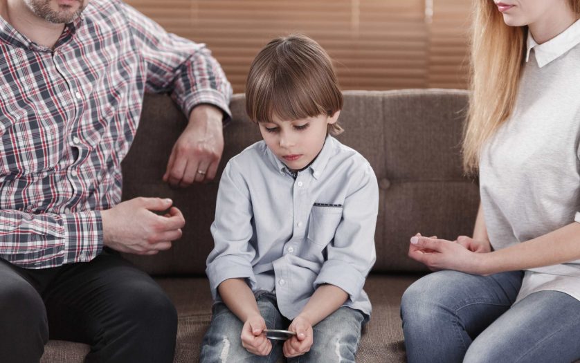 Close-up of boy with autism sitting between worried mother and father